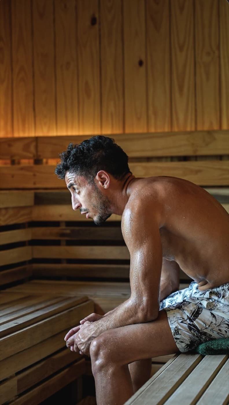 The warm wooden interior of a Finnish sauna with a heater and stones, set up next to a cold plunge for contrast therapy.